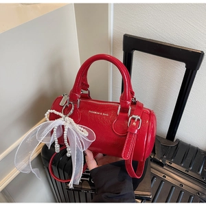 Détail du sac baril rouge en cuir brillant avec nœud en perles et rubans élégants