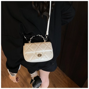 Detail shot of a white quilted crossbody bag with metal chain handle and turn-lock closure