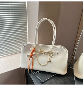 Detail of a beige leather tote bag featuring a metal buckle and colorful orange braided charm