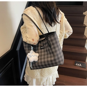 Plaid tote bag with black straps and a plush star pendant worn on a model's shoulder