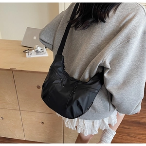 Close-up of black crescent crossbody bag featuring dual zippers and metal ring pulls