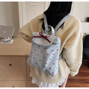 Detail of light blue backpack with red bow prints and heart pendant in a lifestyle setting