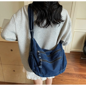 Detail shot of blue denim hobo bag featuring triple front zipper pockets and wide strap
