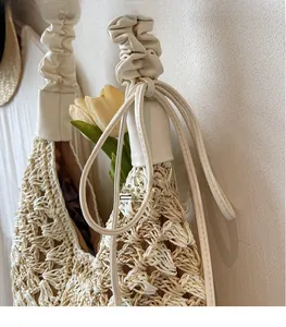 Detail of hand-woven straw tote bag with elegant cream texture and ruched shoulder strap