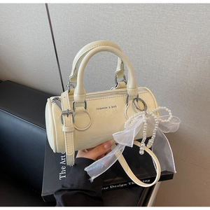 Vue détaillée du sac cylindre crème avec nœud en perles et poignée en cuir