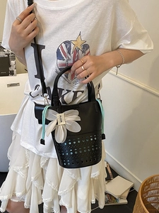 Sac seau noir ajouré avec pendentif floral présenté dans un décor minimaliste