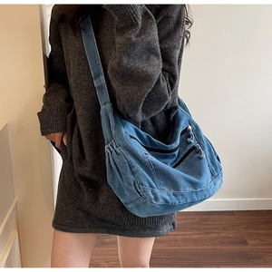 Detail of blue denim hobo bag showing three parallel zipper pockets and washed texture