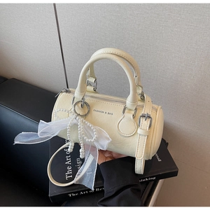 Détail du sac cylindre crème avec perles, nœud en organza et bandoulière ajustable