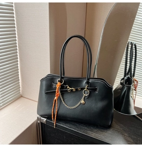 Detail of black leather tote bag featuring orange braided cord and gold chain accent