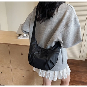 Model wearing a black nylon crossbody bag with multiple zippers and adjustable strap