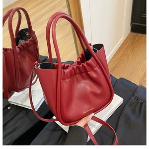 Close-up of wine red leather bucket bag with pleated drawstring and gold logo detail