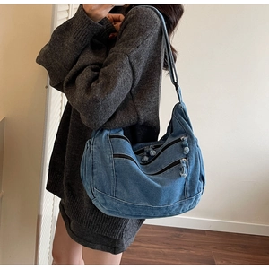 Detail of blue denim crossbody bag with multiple black zipper pockets and wide shoulder strap