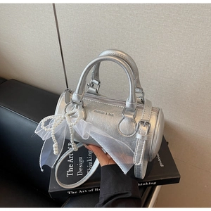 Détail d'un sac cylindrique argenté avec pendentif nœud perlé et logo en relief