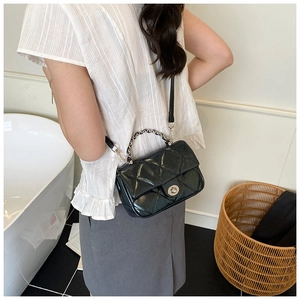 Detail of black quilted crossbody bag with silver twist lock and woven chain handle