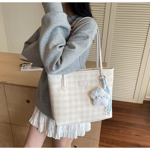 Detail of checkered tote bag with plush cat charm worn by model in a modern room