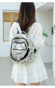 Détail du sac à dos blanc avec motifs de papillons noirs et plusieurs poches dorées zippées