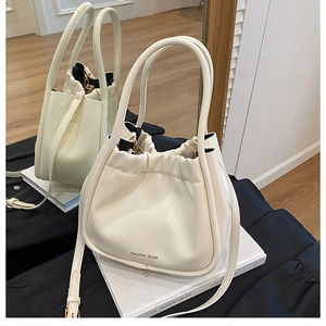 Close-up of cream drawstring bucket bag with gold lettering and adjustable strap