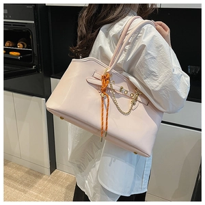 Detailed side view of a large pink faux leather tote bag with orange woven knot and gold chain