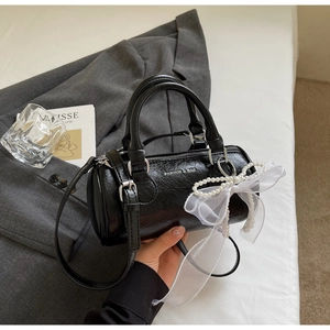 Détail du sac cylindrique noir avec chaîne de perles, nœud organza et texte blanc