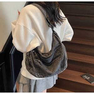 Detail view of large denim hobo bag with multiple zippers worn by a model on stairs