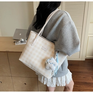 Detailed close-up of cream plaid tote bag with plush kitten charm and brand logo