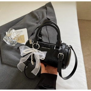 Détail du sac seau cylindrique noir avec nœud en dentelle perlé et logo texte blanc