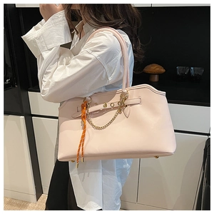 Detail of pink faux leather tote bag featuring metal chains and woven tassel charm