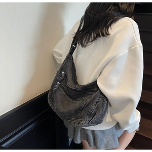 Detail of retro washed denim hobo bag with multiple zipper pockets on female model