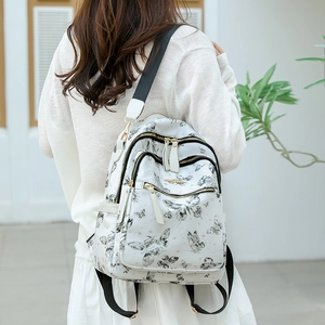 Détail du sac à dos blanc avec motifs de papillons noirs et compartiments zippés