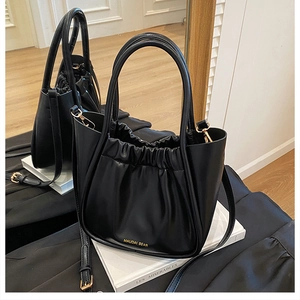 Detail view of black pleated bucket bag with gold hardware and cylindrical handles