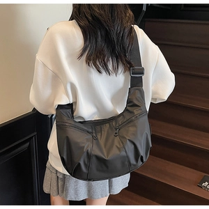 Detailed back view of a black multi-pocket crossbody bag with metallic zippers on a model