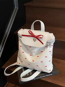 White leather bucket backpack featuring a 3D red bow and heart pendant on wood stairs