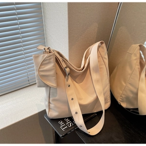 Detail of a beige nylon tote bag with metal eyelet strap and a mini decorative pouch