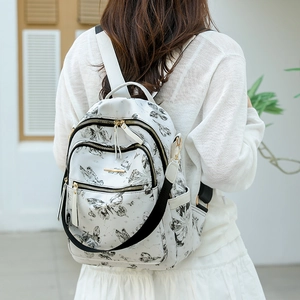 Vue arrière d'une femme portant un sac à dos blanc avec des motifs papillons et constellations