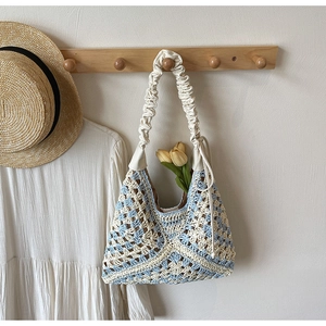 Detail of blue and white crochet floral pattern on a knit hobo bag with gathered strap