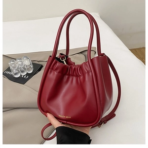 Close-up of deep red pleated bucket bag with golden logo and soft leather texture