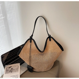 Detail of handwoven straw tote with black leather trim and heart charm on a stool