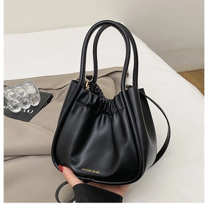 Detailed view of black pleated bucket bag with dual handles and gold brand lettering