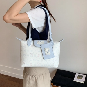 Detail of white tote bag with cute cartoon prints and light blue straps worn by a model