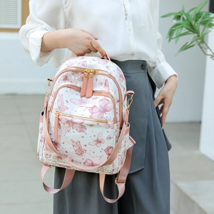 Détail du sac à dos crème avec imprimé papillon violet et plusieurs poches zippées dorées