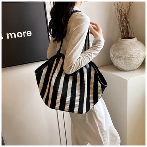 Detail of a large black and white striped tote bag with leather straps on a model's shoulder