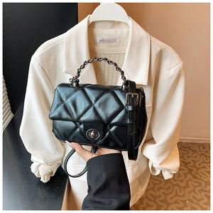 Close-up of black quilted leather texture and metal chain strap on crossbody bag