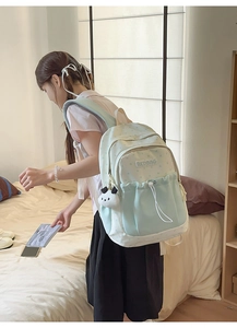 Detail of mint green student backpack with panda plush charm and brand patch shown on model