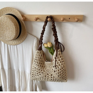 Detail of hollow woven pattern on beige straw bag with brown pleated shoulder strap