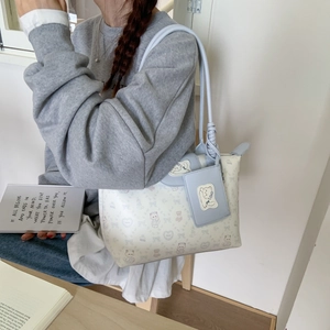 Detail of light beige tote bag with blue cat and bow patterns worn by a model