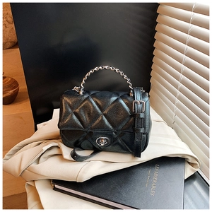 Detail of black quilted leather crossbody bag featuring metal chain and turn-lock closure