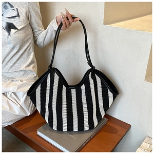 Detail of fan-shaped striped tote bag with black leather straps on a wooden bench