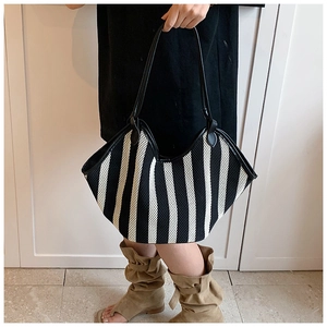 Detail view of a large black and white striped woven tote bag with leather handles