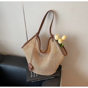 Detail of a large straw tote bag with brown leather trim and beige woven texture