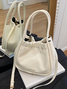 Elegant cream bucket bag with drawstring closure and gold hardware on white book